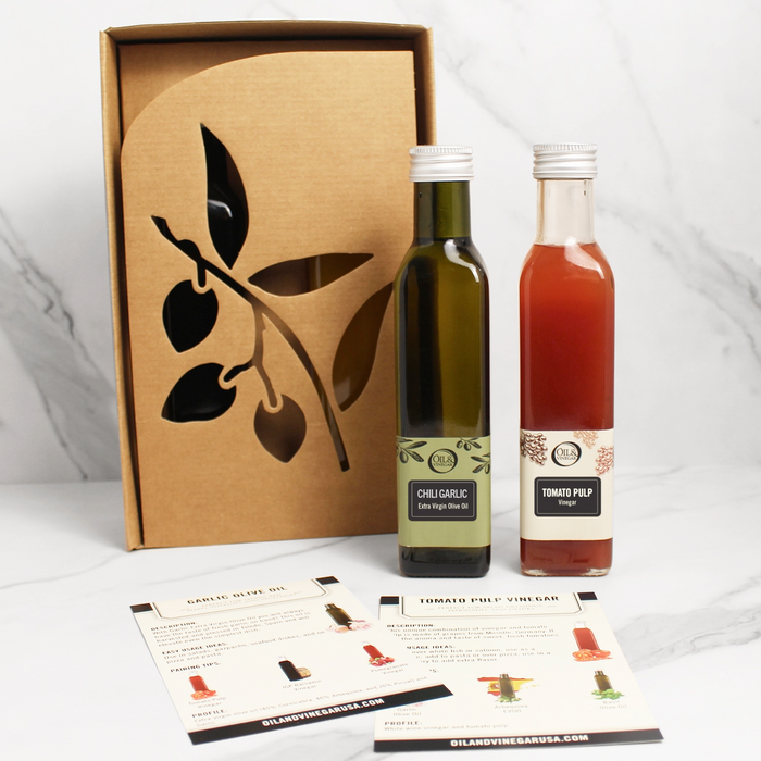 Two bottles, one olive oil and one vinegar with a box featuring an olive design on a white background.