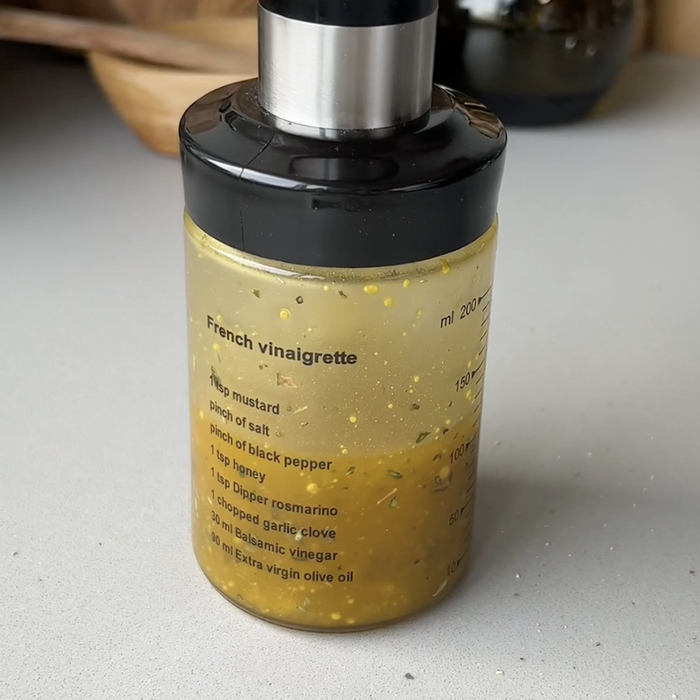 Up close image of a dressing shaker filled with oil, vinegar, and herbs with a recipe printed on the side for a french vinaigrette.