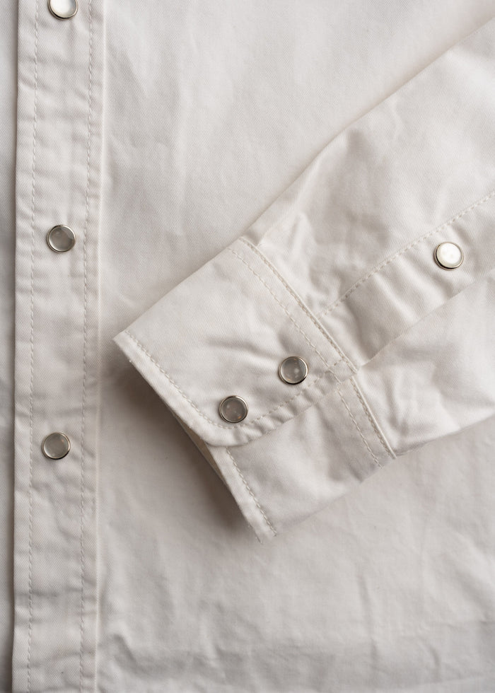 White shirt with metal snap buttons on the cuff and front, showcasing detailed stitching and smooth fabric texture.