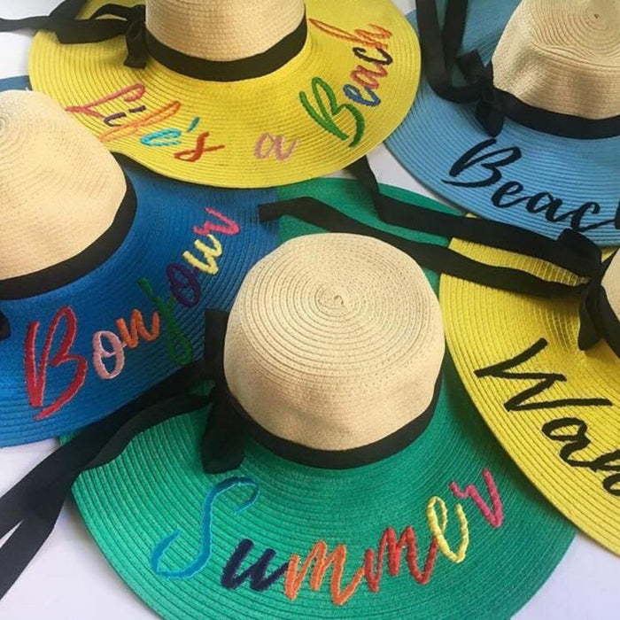 Collection of colorful hand-painted straw hats with summer and beach-themed designs and black ribbon bands