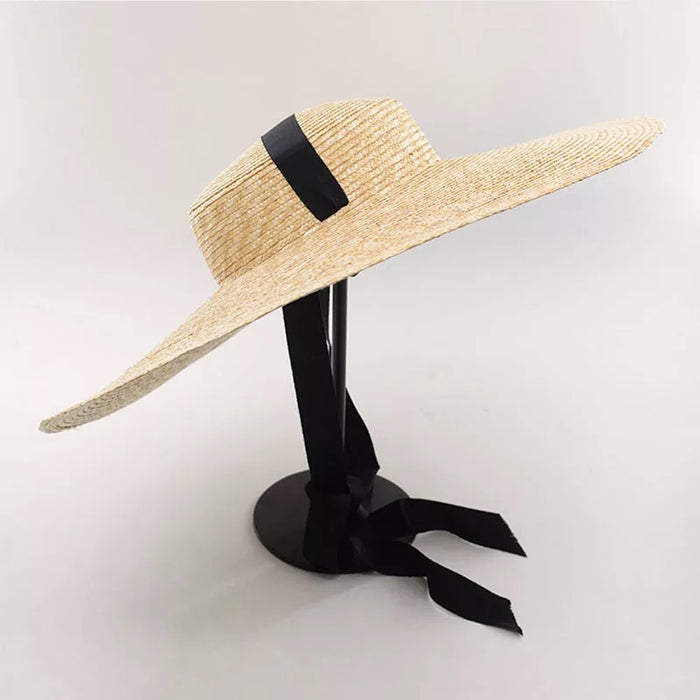 Large wheat straw hat with wide brim and black ribbon band on display stand