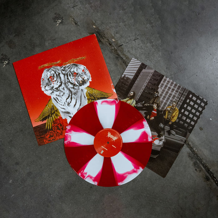 Square vinyl with a red background and a two headed white tiger with gold wings with red roses at the bottom of the cover, blood coming from both tiger’s eyes, and a crown of thorns above both of the tigers heads. There is a vinyl record that is next to the vinyl cover that is the colors red and white. There is also a picture of the band members sitting on top of a car underneath both the vinyl and vinyl cover. The image is taken with a concrete sidewalk background.