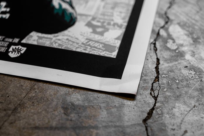 A close-up of a damaged Bane 18x24 black-and-white poster on cracked concrete, showing the paper’s edge and part of a white border.