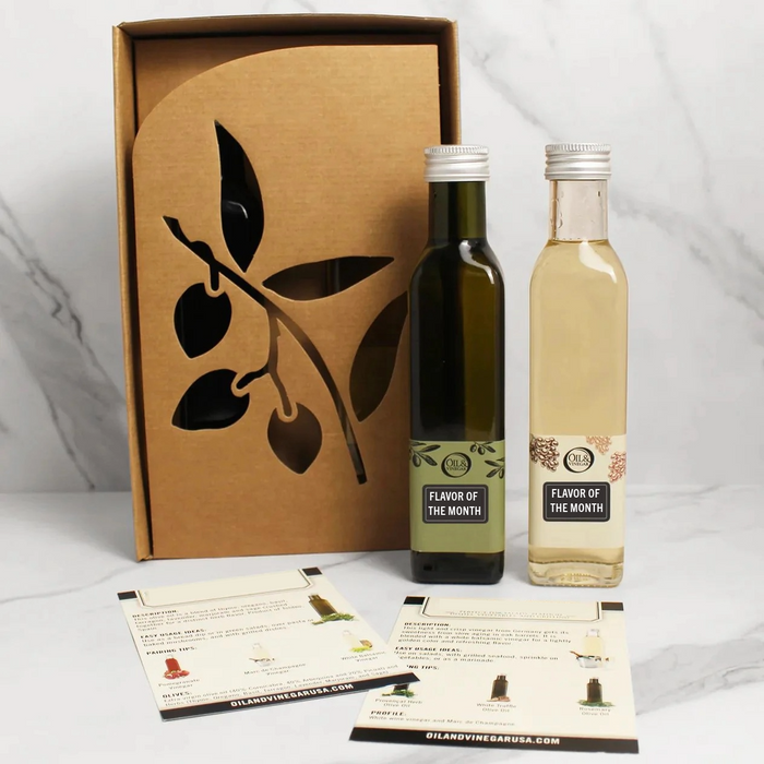 Two bottles of gourmet food items, both labeled as Flavor of the month, and are presented alongside their packaging box with a leaf design. There are also informational cards in front of the bottles.