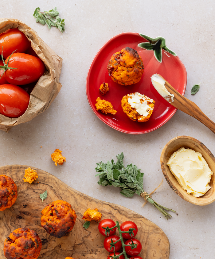 Tomato rolls and tomatoes on a red plate with small round dishes, and a wooden board with more round dishes on a light gray background.