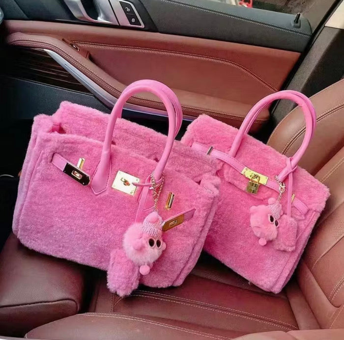 Two pink fluffy handbags with gold hardware on a car seat.