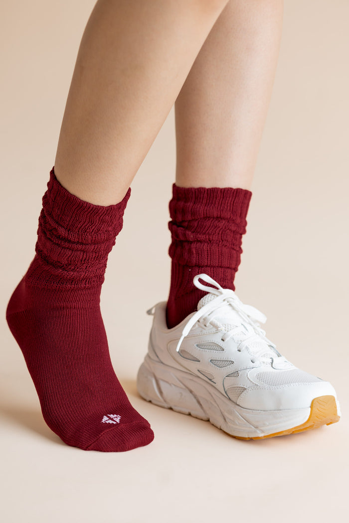 Model wearing Adult Scrunch Socks in Ruby and a white sneaker on one foot on a beige background