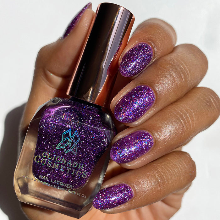 Close-up of nails painted with Armadillo's Night Out Nail Lacquer on Medium skin tone. Hand is holding polish bottle.