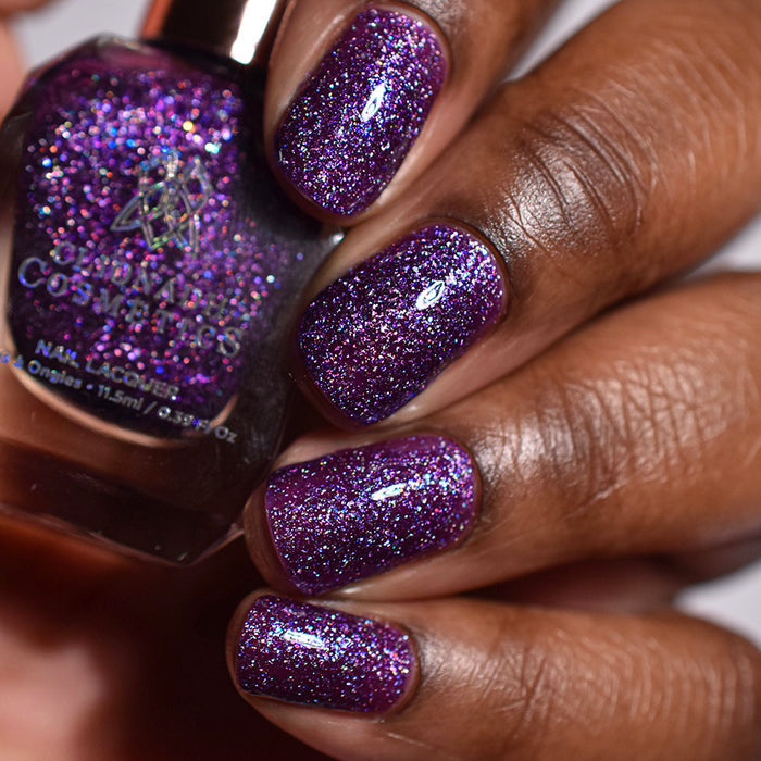 Close-up of nails painted with Armadillo's Night Out Nail Lacquer on  deep skin tone. Hand is holding polish bottle.