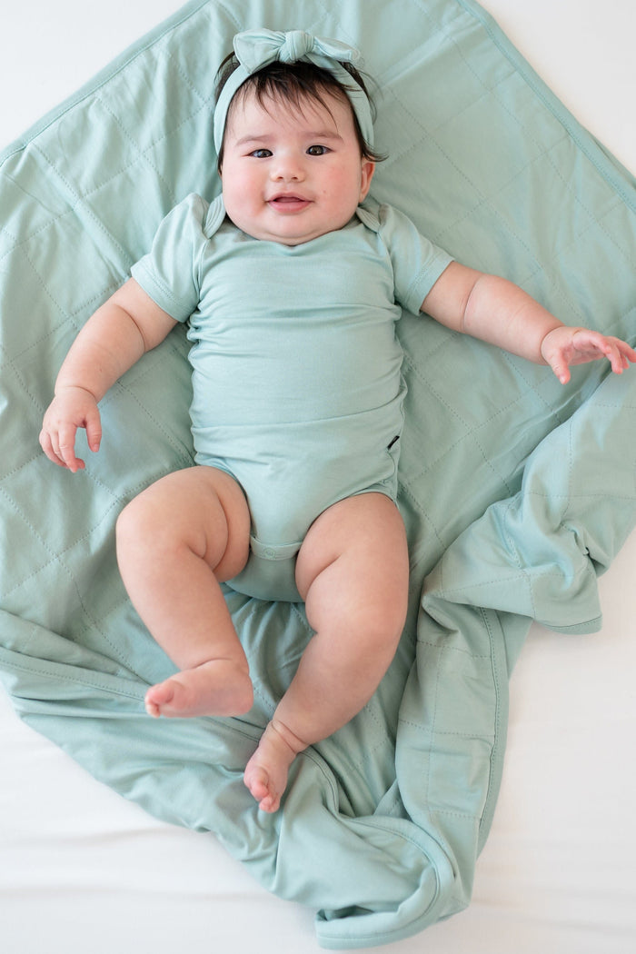 Baby in Sage bodysuit laying on Baby Blanket in Sage 1.0