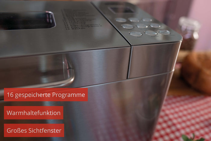 Eine Nahaufnahme des Unold Backmeister® Edel Edelstahl-Brotbackautomaten mit Bedientasten und großem Sichtfenster; Deutsche Text-Highlights: 16 gespeicherte Programme, Warmhaltefunktion, großes Sichtfenster.