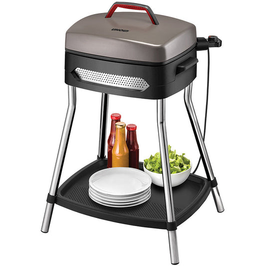 Der Unold Barbecue Power Grill steht auf stabilen Metallbeinen mit Metallic-Finish und geschlossenem Deckel und verfügt über eine untere Ablage, auf der vier weiße Teller, drei Gewürzflaschen und eine Salatschüssel Platz finden.