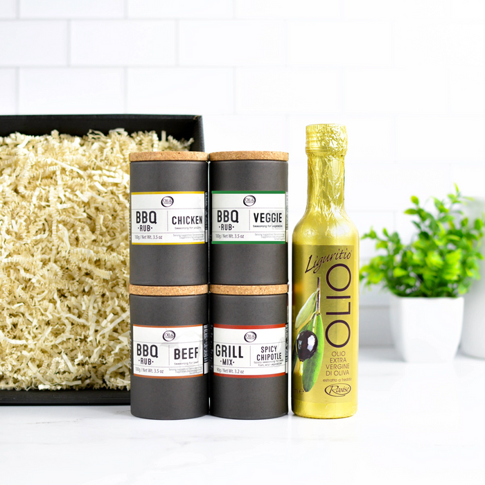 Three cylindrical BBQ seasoning containers and a bottle of olive oil on a white surface with a plant in the background.