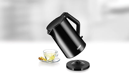 Der Unold Blitzkocher Design 1,4 L in schlichtem Schwarz steht schräg über einer Teetasse aus Glas mit Zitronenscheibe, neben seinem runden Sockel auf einer weißen Fläche mit unscharfem Hintergrund.