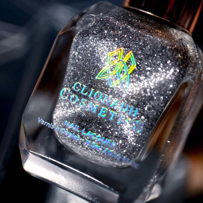 Angled, close-up of Broken Mirror Nail Lacquer bottle, on a blurred background.
