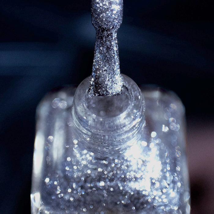 Close-up of nail polish bottle and brush showing product Broken Mirror Nail Lacquer, on a dark blurred background.