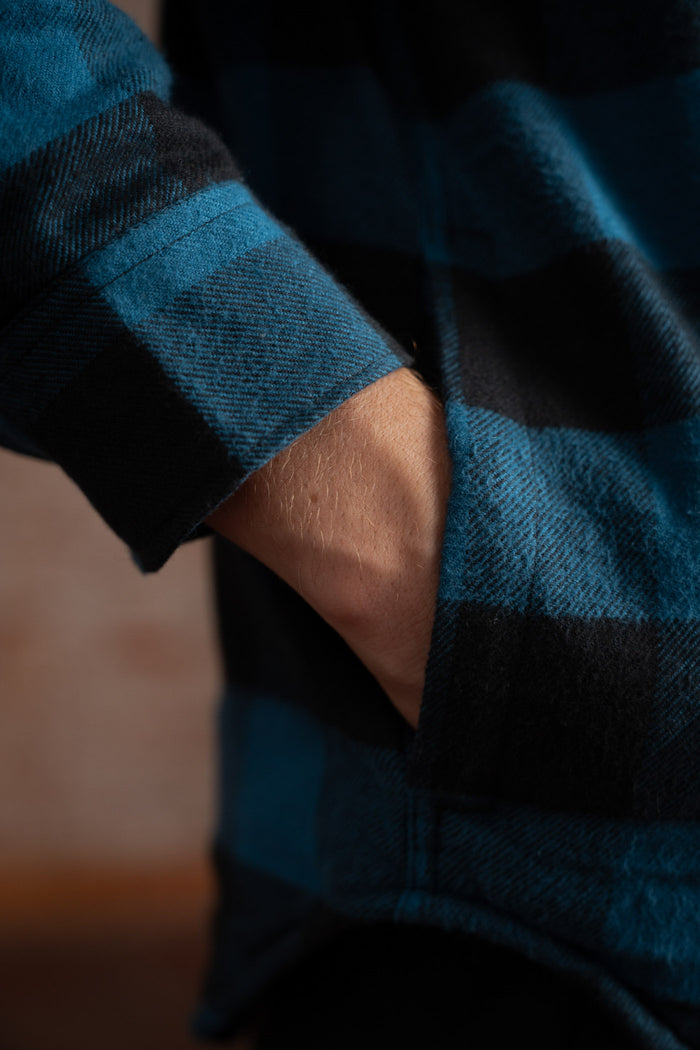 A hand rests in the pocket of a blue and black plaid flannel shirt, highlighting the cozy texture and casual style.