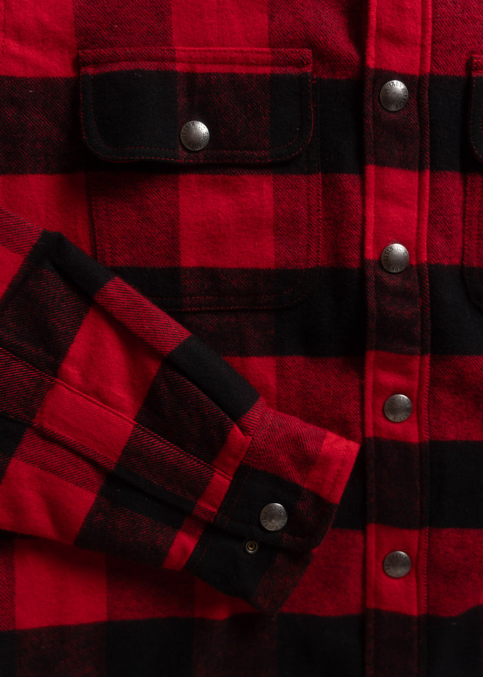 Close-up of a red and black plaid flannel shirt with metal snap buttons and chest pockets, showcasing its classic design.