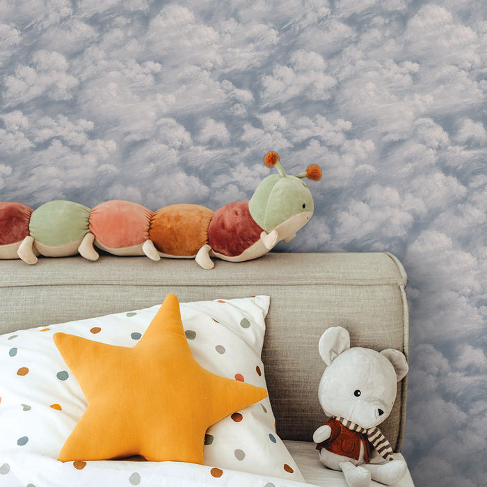 Tempaper's Clouds Peel And Stick Wallpaper in light blue shown in a kids bedroom behind a bed with stuffed animals.