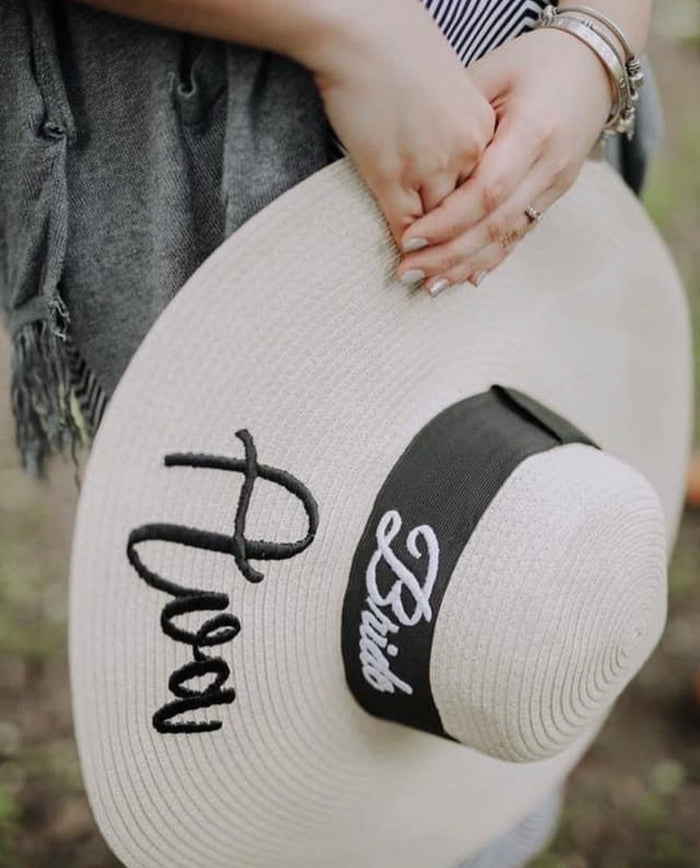 Custom prenuptial hat set with bride embroidery and wide brim held by person wearing bracelets