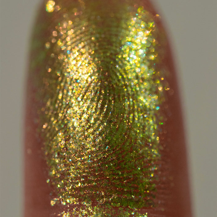 Close-up finger swatch of Dais Eyeshadow on deep skin tone, on a grey background.