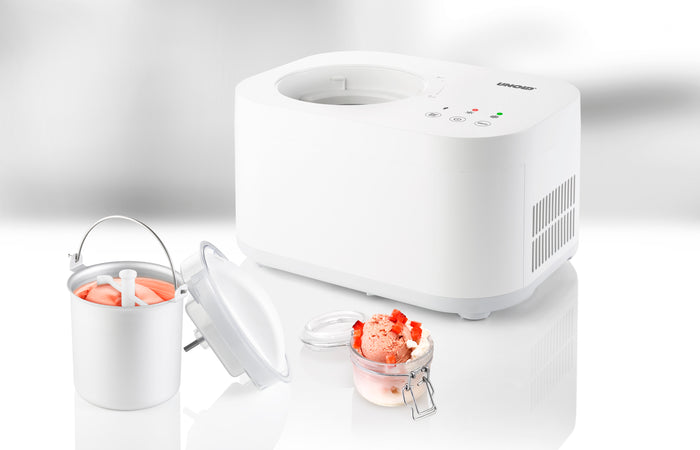 Die Unold Eismaschine Snow 1 L steht ohne Metallschüssel und Deckel neben einem Glas mit rosa Fruchteis auf einer glänzend weißen Oberfläche.