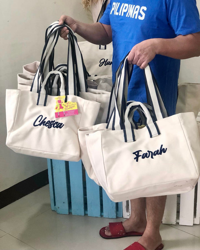 Travellers Hat Boutique embroidered boat tote bag in white with navy striped handles and personalized names Chesca and Farah
