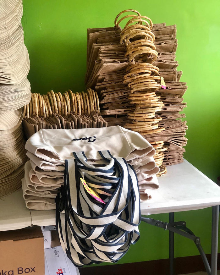 Stack of canvas embroidered boat tote bag with striped handles on a white table at Travellers Hat Boutique