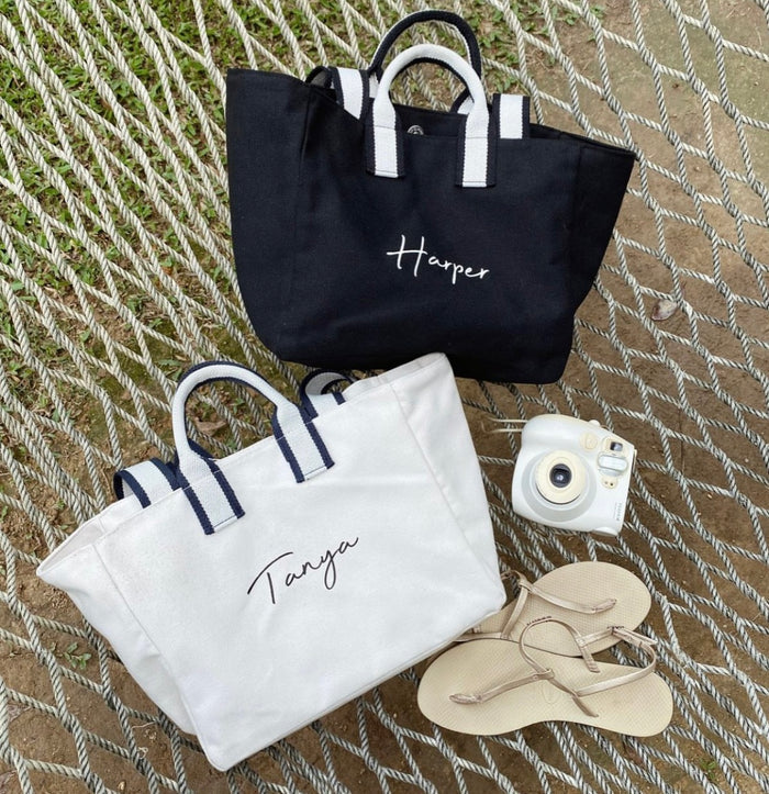 Embroidered boat tote bag in black and white with personalized names displayed on a net background