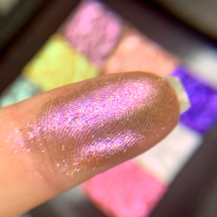 Close-up finger swatch of the eyeshadow Entropy on fair skin tone. Blurred palette in the background.