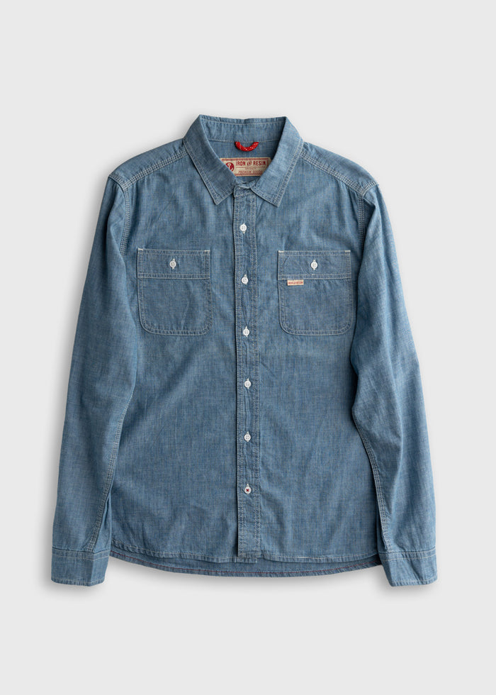Blue denim button-up shirt with two chest pockets, laid flat on a light gray background, showcasing casual style and texture.