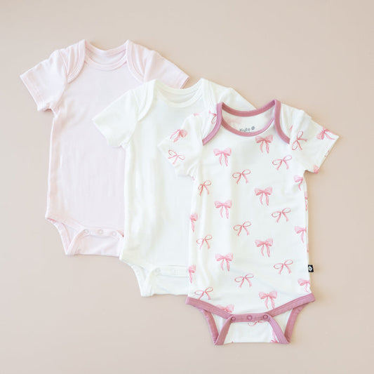Three baby bodysuits on a beige background