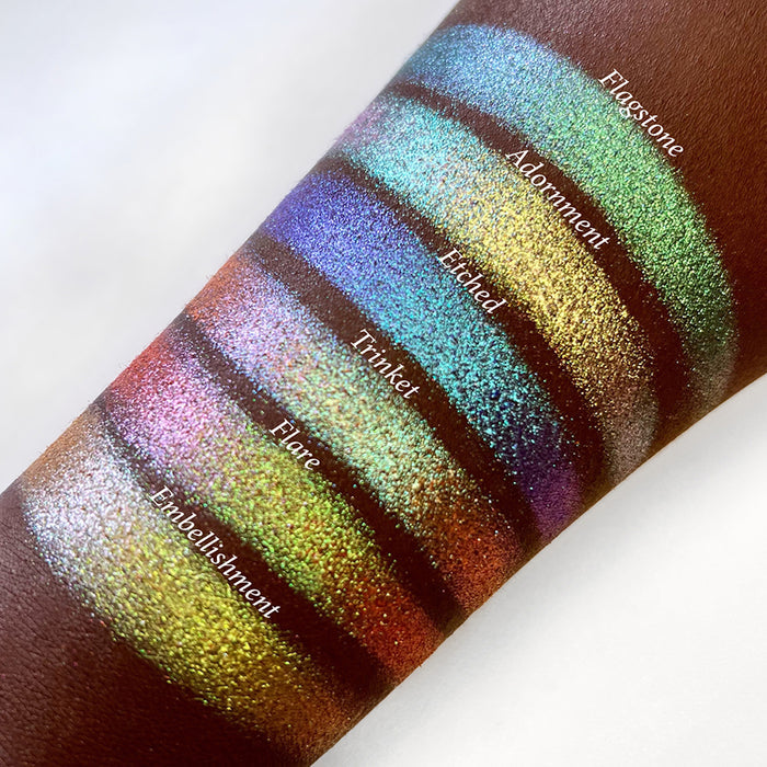 Top angled arm swatches on deep skin tone of Flare Glitter Multichrome Eyeshadow shifts compared to Flagstone, Adornment, Etched, Trinket and Embellishment