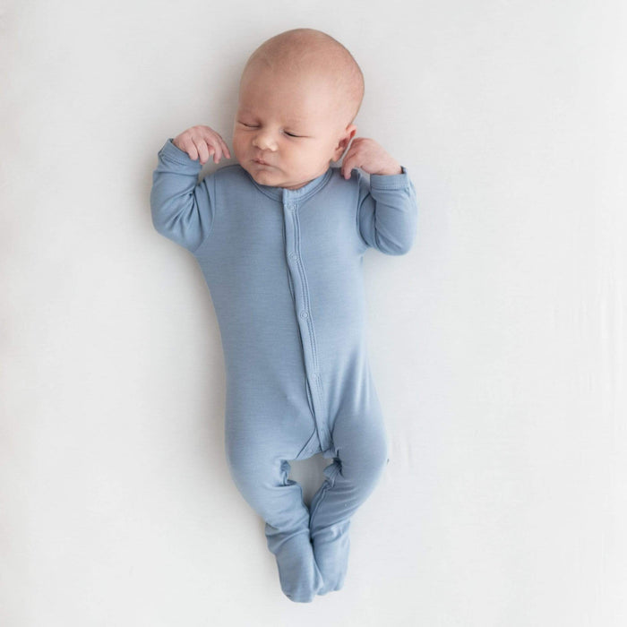 Sleeping newborn with arms up and wearing Kyte Baby Footie in Slate