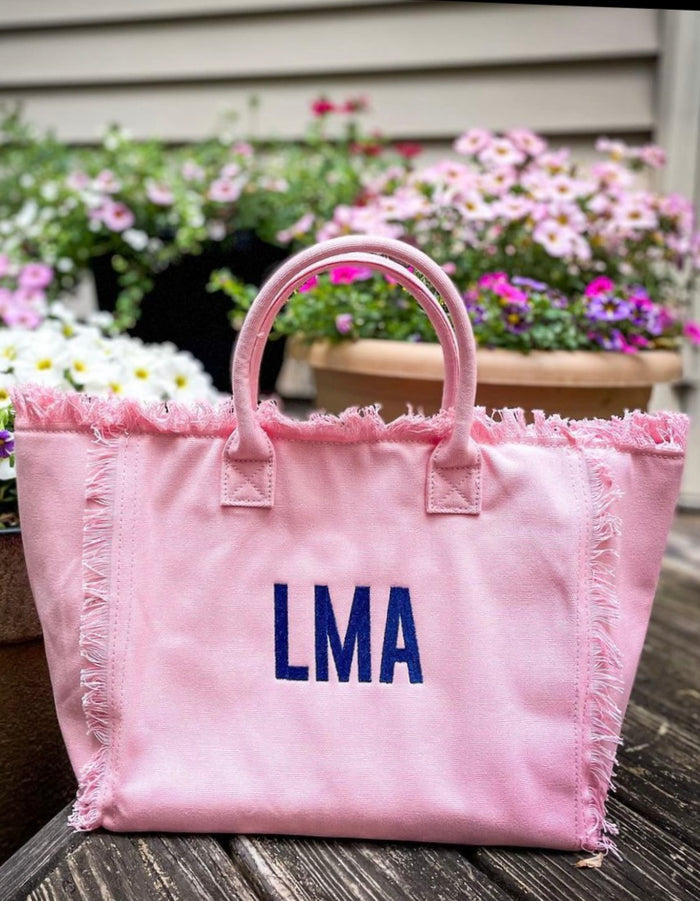 Pink personalized canvas tote with fringe featuring blue LMA monogram from Travellers Hat Boutique