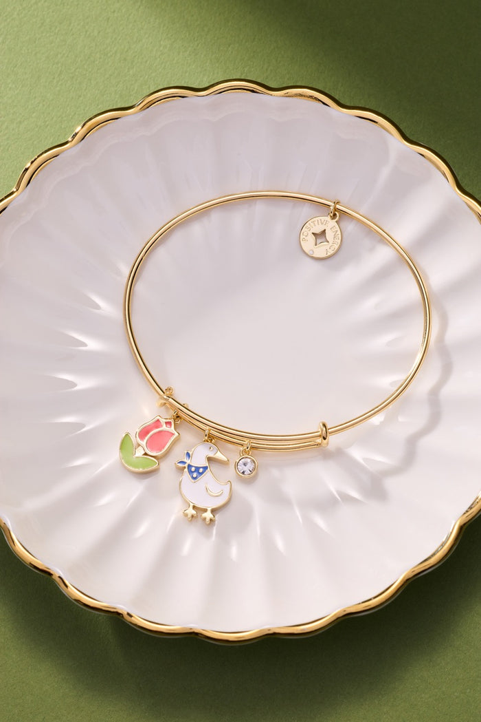 Gold bracelet with charms on a decorative white plate with gold rim against a green background