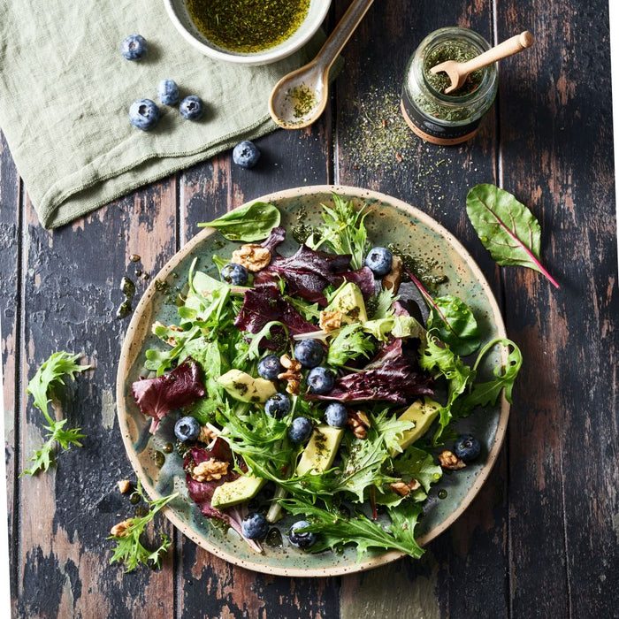 Salatgewürz im Korkenglas neben einem Sommersalat auf einem Tonteller.