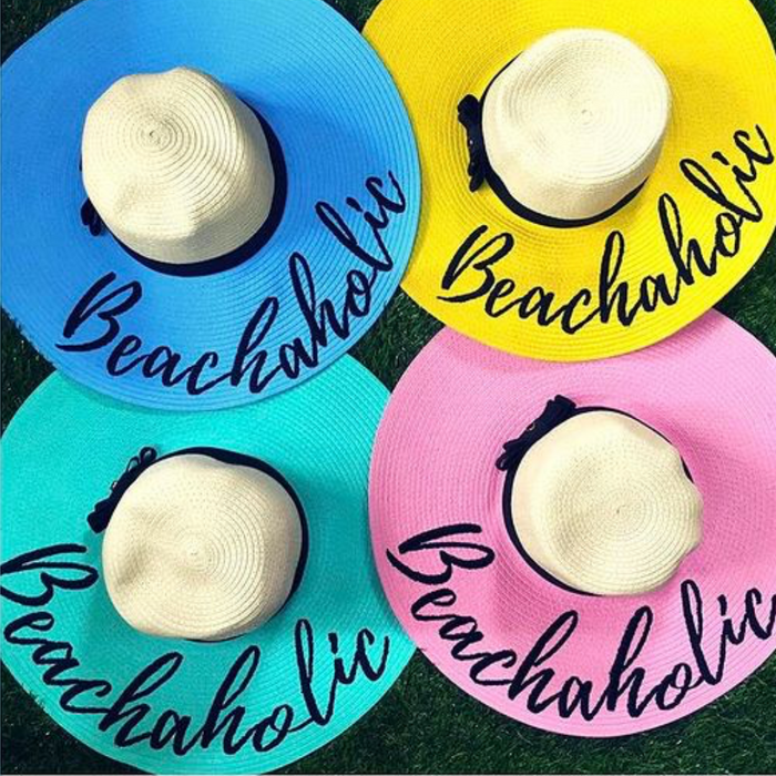 Colorful hand-painted straw hat collection with Beachaholic text from Travellers Hat Boutique