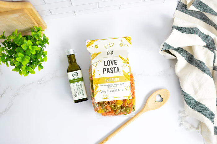 Packaged pasta with a bottle of olive oil and a wooden spoon on a white surface.