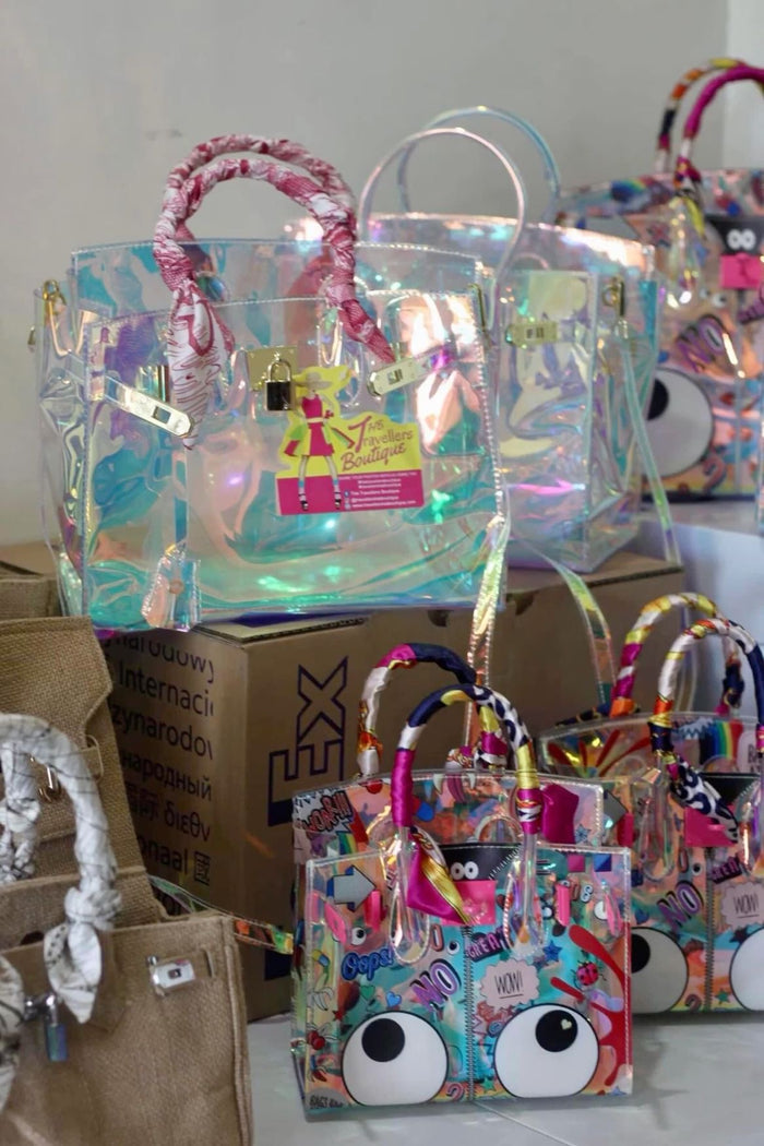 Holographic clear tote bag from Travellers Hat Boutique with pink wrapped handles on display