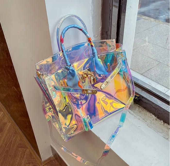 Holographic clear tote bag with blue handles from Travellers Hat Boutique displayed on a windowsill
