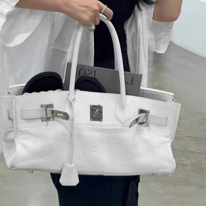 A person holding a white handbag with silver hardware.