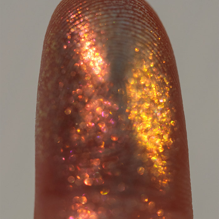 Close-up finger swatch of  Incandescence Eyeshadow on deep skin tone, on a grey background.