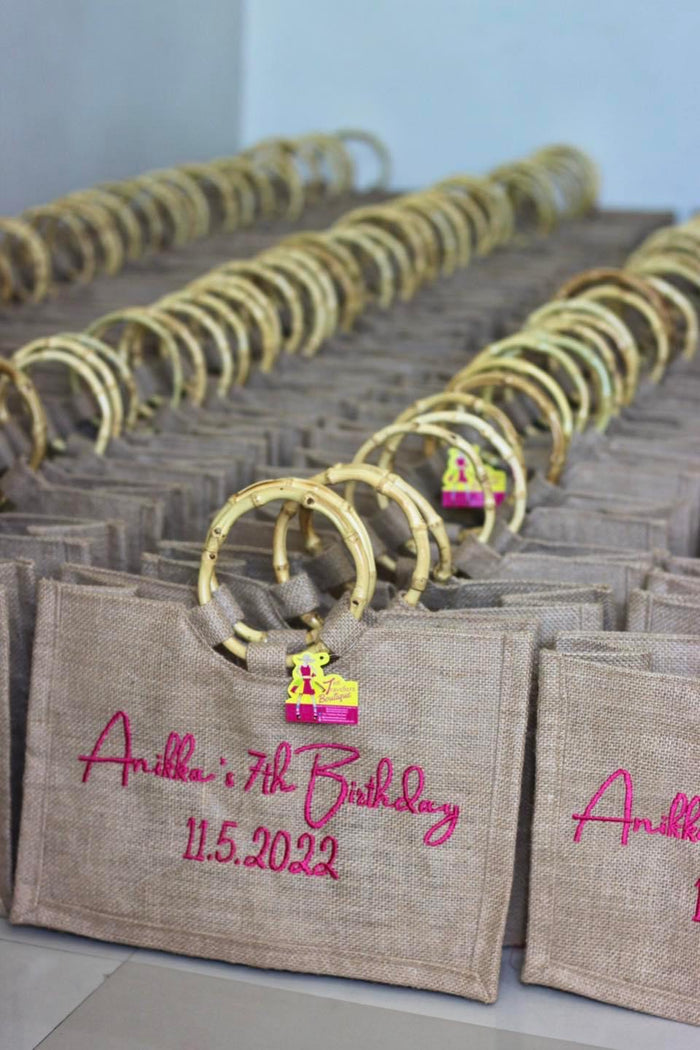 Jute tote bags with bamboo handles featuring pink embroidery for a birthday event by Travellers Hat Boutique
