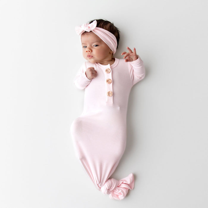 Newborn baby in a light pink knotted gown and matching bow headband