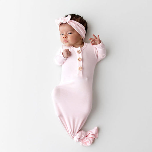 Newborn baby in a light pink knotted gown and matching bow headband