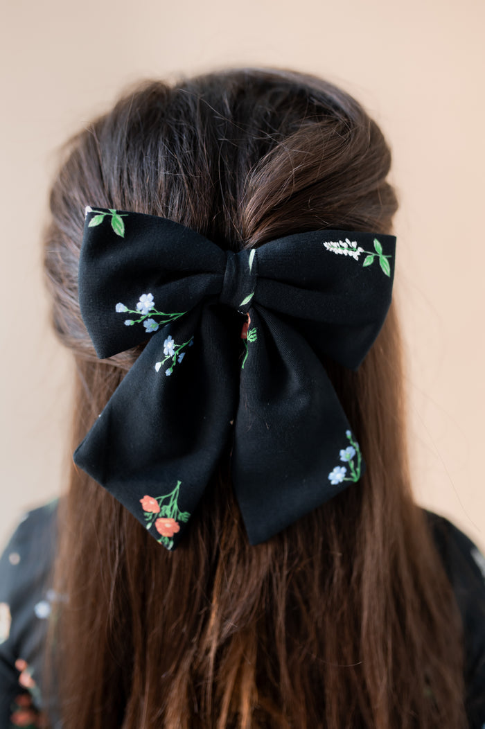 Girl wearing Large Alligator Clip Bow in Midnight Wildflower print in hair on a beige background