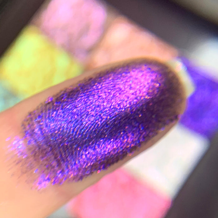 Close-up finger swatch of the eyeshadow Liquidus on fair skin tone. Blurred palette in the background.