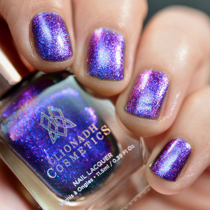 Close-up of nails painted with Liquidus Nail Lacquer on fair skin tone. Hand is holding polish bottle.