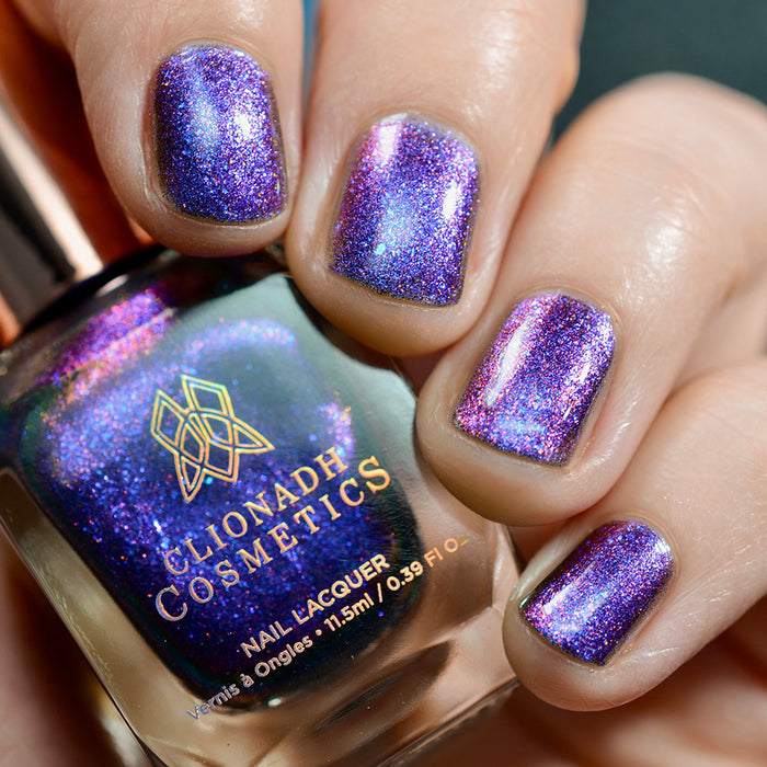 Close-up of nails painted with Liquidus Nail Lacquer on fair skin tone. Hand is holding polish bottle.